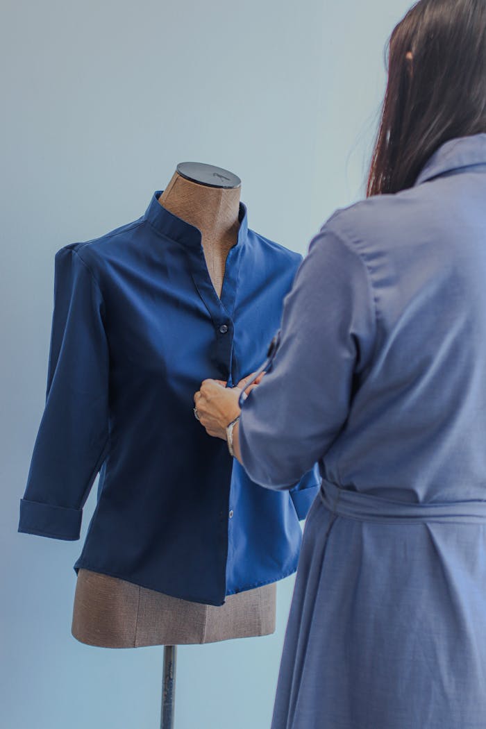 Female tailor in blue adjusting a blue shirt on a mannequin indoors.