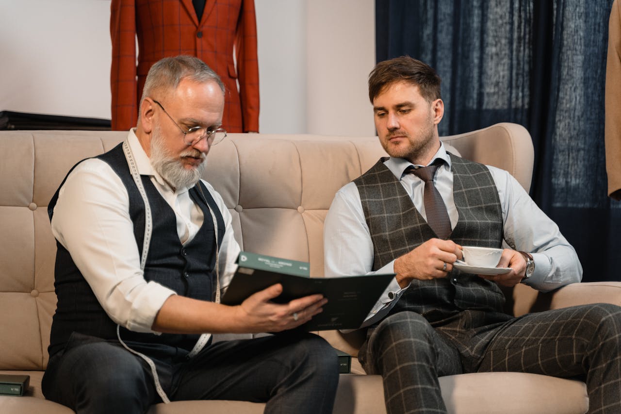 Tailor and client reviewing fabric samples for a custom suit in a stylish workshop.